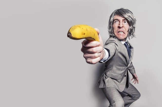 picture of grumpy man pretending banana is a gun